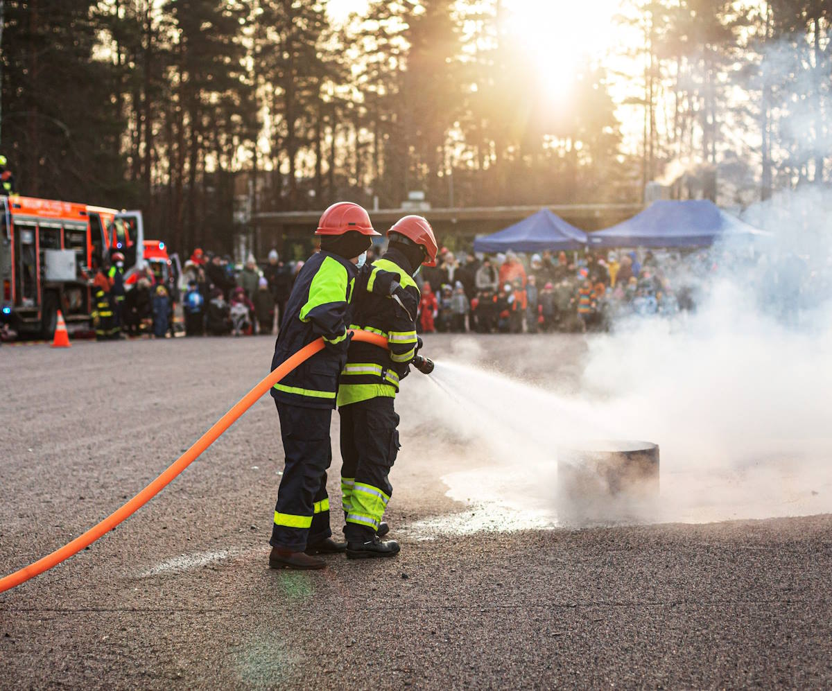 Kuva Paloturvallisuusviikon Päivä Paloasemalla -tapahtumasta Haagassa vuonna 2021. Kuvassa kaksi lasta, joilla on suojavaatteet päällä. Lapset sammuttavat letkulla palavaa tynnyriä.