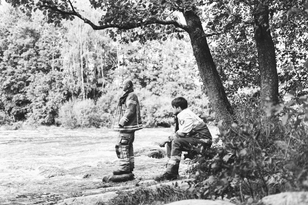 Kuvituskuva. Kuvassa kaksi pelastusasuun pukeutunutta henkilöä tuijottaa järvelle metsäisällä rantatörmällä. Kuva: Teemu Heikkilä. 