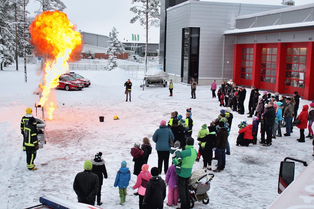 Kuvassa Päivä Paloasemalla -tapahtumaan osallistuneet perheet seuraavat talvisella paloaseman pihalla näytöstä, jossa sammutetaan suurta paloa. Palon liekit ovat monien metrien korkuiset.