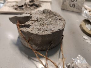 Pyöreä harmaa betonilohkarenäyte joka on lohjennut räjähdysmäisesti.
